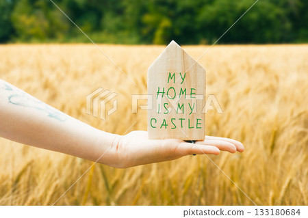 Hand holding a wooden house sign that says My home is my castle. Hand holding a wooden house sign that says My home is my castle. 133180684