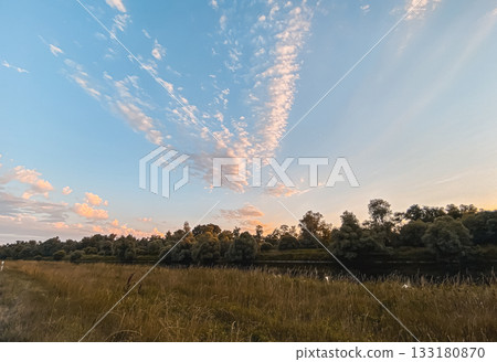 Serene landscape with vibrant clouds reflecting over tranquil river at sunset with lush greenery Serene landscape with vibrant clouds reflecting over tranquil river at sunset with lush greenery 133180870