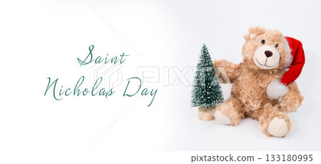 Cute teddy bear wearing Santa hat holding small Christmas tree with festive holiday spirit Cute teddy bear wearing Santa hat holding small Christmas tree with festive holiday spirit 133180995