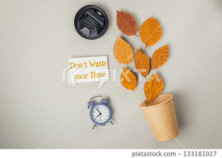 Creative flat lay arrangement with autumn leaves, clock, and motivational quote on a neutral background 133181027