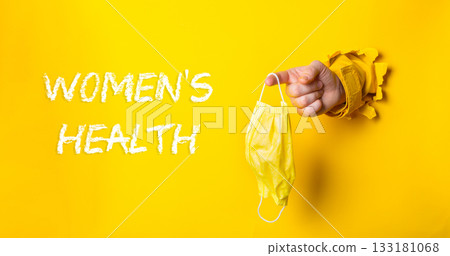 Hand holding a yellow mask with the words womens health written below it 133181068