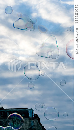 Colorful soap bubbles floating against a cloudy sky with buildings in the background Colorful soap bubbles floating against a cloudy sky with buildings in the background 133181072