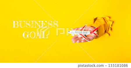 Hand holding airplane model against vibrant yellow background with business goal concept 133181086