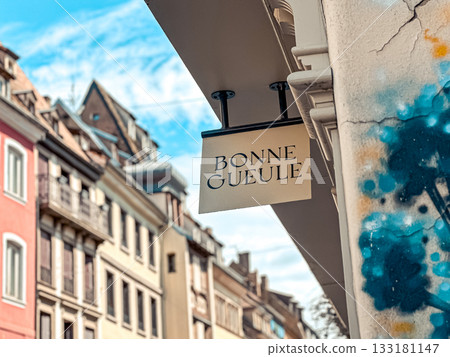 Urban street scene featuring a shop sign with artistic graffiti on a building, showcasing vibrant architecture and a clear blue sky in the background 133181147