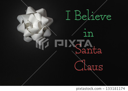 White gift bow on dark background with festive text expressing belief in Santa Claus White gift bow on dark background with festive text expressing belief in Santa Claus 133181174