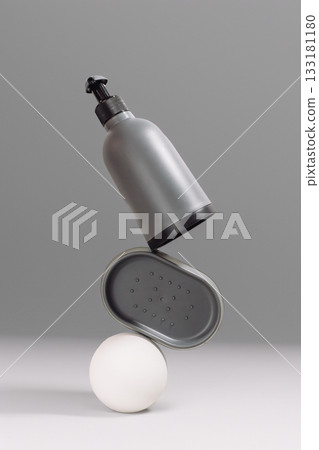 Gray cosmetic bottle and container balanced on a white sphere against a minimalist background 133181180
