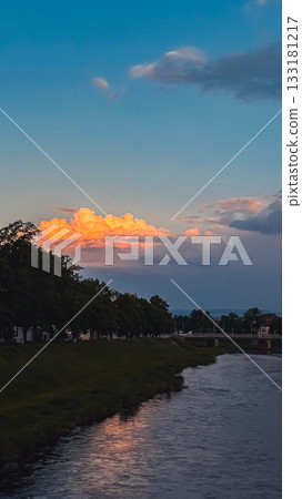 Serene river landscape with vibrant sunset clouds reflecting on calm water surface Serene river landscape with vibrant sunset clouds reflecting on calm water surface 133181217