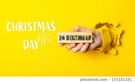 Hand holding wooden block with date 24 December, celebrating Christmas Day with vibrant yellow background Hand holding wooden block with date 24 December, celebrating Christmas Day with vibrant yellow background 133181281