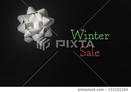 White gift bow on dark background with colorful text promoting winter sale and holiday spirit White gift bow on dark background with colorful text promoting winter sale and holiday spirit 133181284