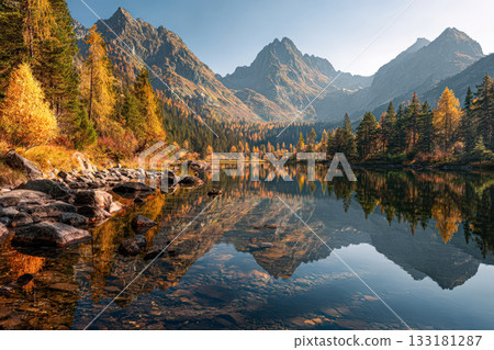 Serene mountain landscape with autumn foliage reflecting in calm lake water at sunrise 133181287