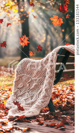 Cozy knitted blanket draped over a bench surrounded by colorful autumn leaves in a serene park 133181544