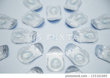 A creative layout in the form of a three-dimensional flower lies in one-day contact lenses in disposable protective packaging, in the center there is a transparent contact lens on a white background A creative layout in the form of a three-dimensional flower lies in one-day contact lenses in disposable protective packaging, in the center there is a transparent contact lens on a white background 133181885