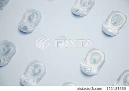 Top view of the diagonal layout of one-day contact lenses in disposable protective packaging and in the center a transparent contact lens on a white background. The concept of ophthalmology, vision 133181886