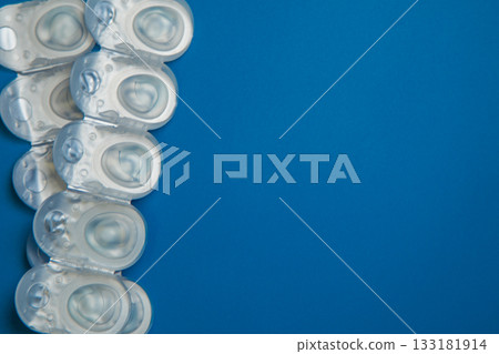 Many daily contact lenses in a disposable protective case in which clear lenses float lie on the side on a blue background with space for text. The concept of ophthalmology, vision correction, eye 133181914