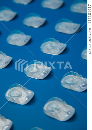 A top view of one-day contact lenses in a disposable protective case lying on a blue background at the same distance. The concept of ophthalmology, vision correction, eye care. High quality photo A top view of one-day contact lenses in a disposable protective case lying on a blue background at the same distance. The concept of ophthalmology, vision correction, eye care. High quality photo 133181917