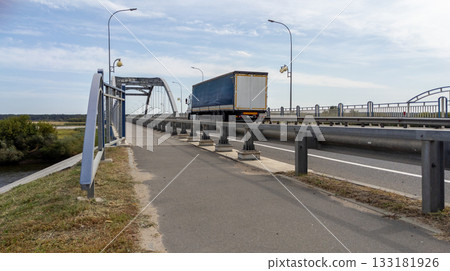 Large truck enters a river bridge against a blue cloudy sky. Concept for freight transportation and trade. 133181926