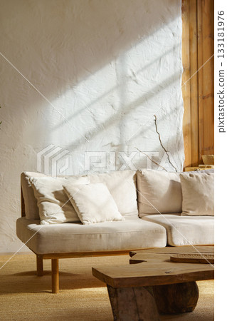 Modern minimalist interior of living room with beige sofa, rustic wooden table in natural sunlight 133181976