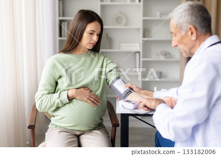 Male doctor measuring blood pressure of pregnant woman during appointment in clinic Male doctor measuring blood pressure of pregnant woman during appointment in clinic 133182006