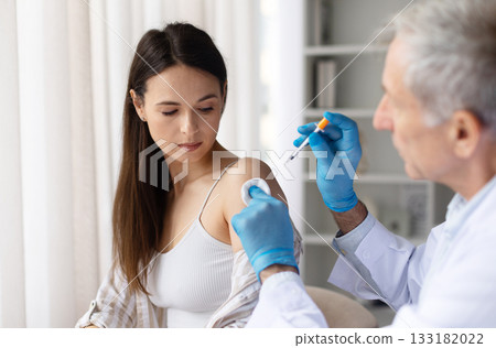Female patient receiving vaccine injection from male doctor wearing gloves in clinic 133182022