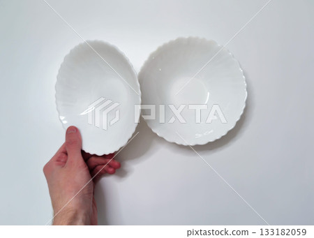 Hand Holding White Porcelain Plate with Wavy Edge on Light Background Hand Holding White Porcelain Plate with Wavy Edge on Light Background 133182059