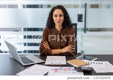 Confident businesswoman with arms crossed at her desk, serious and focused amid laptop, documents and financial charts, conveying professionalism, leadership and corporate success in office Confident businesswoman with arms crossed at her desk, serious and focused amid laptop, documents and financial charts, conveying professionalism, leadership and corporate success in office 133182076