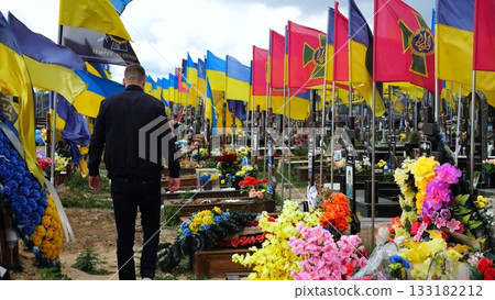 Mourning man go among countless graves of ukrainian soldiers with national flags at military cemetery in Kharkiv. Scene reflects personal sorrow and nation collective loss caused by russian aggression Mourning man go among countless graves of ukrainian soldiers with national flags at military cemetery in Kharkiv. Scene reflects personal sorrow and nation collective loss caused by russian aggression 133182212