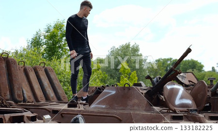 Young man looking at destroyed military equipment of the russian army. Exhibition of rusty and burned-out armored vehicles on ukrainian territory. War between Ukraine and russia. Slow motion Young man looking at destroyed military equipment of the russian army. Exhibition of rusty and burned-out armored vehicles on ukrainian territory. War between Ukraine and russia. Slow motion 133182225