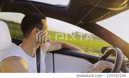 Profile of young handsome man driving a modern electric car with sunlight at background. Young male driver riding on electrical vehicle at countryside. Concept of journey and trip. Close up Profile of young handsome man driving a modern electric car with sunlight at background. Young male driver riding on electrical vehicle at countryside. Concept of journey and trip. Close up 133182230