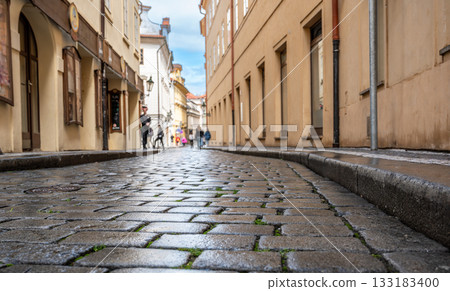 Prague, Czech Republic, August 9, 2023. Conceptual footage with foreground on stone paved street and blurred background people walking on the street. Low point of view, wide angle lens. Prague, Czech Republic, August 9, 2023. Conceptual footage with foreground on stone paved street and blurred background people walking on the street. Low point of view, wide angle lens. 133183400