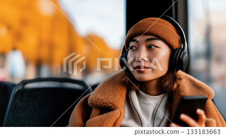 young woman with a smartphone and headphones enjoys an autumn bus ride, copy space with idea of the rhythm of the city and travel, listening to her favorite podcasts or music on her smartphone apps young woman with a smartphone and headphones enjoys an autumn bus ride, copy space with idea of the rhythm of the city and travel, listening to her favorite podcasts or music on her smartphone apps 133183663