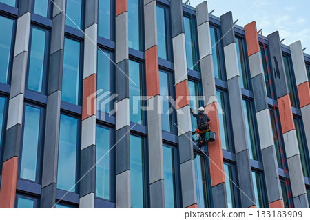 High rise worker cleaning windows on modern building facade 133183909