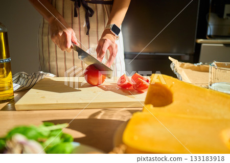 Woman cutting tomato on wooden board in kitchen 133183918