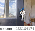 A close-up of keys hanging from a door lock against a blurred background of a private new building. Door and window installation in a private home. 133184174