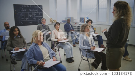 Diverse Adult Learners Sit Modern Desks, Writing and Listening Attentively Teacher Diverse Adult Learners Sit Modern Desks, Writing and Listening Attentively Teacher 133184178