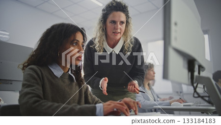 Stylish Mature Female Teacher Walks Through Modern Computer Classroom, Guiding Adult Students 133184183