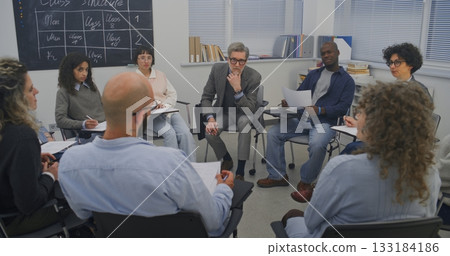 Inside Training Room, Adult Participants Gather in Seated Circle While Instructor Leads Conversation 133184186
