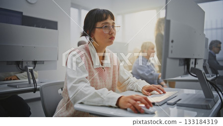 Focused on Screen Woman in Glasses Sits at Computer During Coding Class, Smiling 133184319