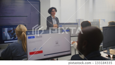 Female Teacher Stands By Large Screen Displaying Programming Code, Explaining Modeling Concepts 133184335