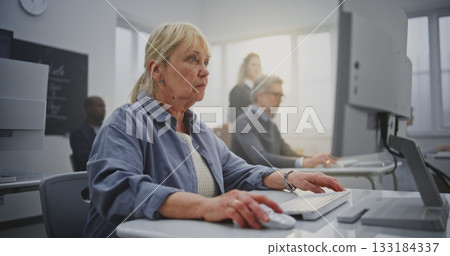 Confident Elderly Woman With Long Blonde Hair Practices Coding in Bright Computer Lab 133184337