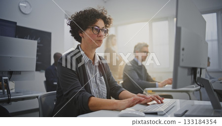 Dark Haired Woman in Her Mid Forties Sits at Monitor Coding During IT Class Dark Haired Woman in Her Mid Forties Sits at Monitor Coding During IT Class 133184354