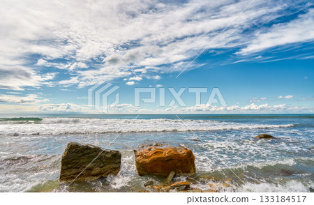 Ocean waves crash energetically against rock fragments, rocks serving as a pedestal for products against a dynamic seascape, a beautiful view of a stormy sea 133184517