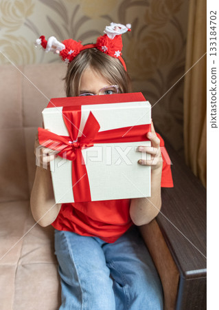A girl in a Santa Claus hat opens a gift. It's Christmas time. 133184702