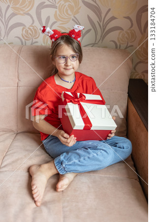 A girl in a Santa Claus hat opens a gift. It's Christmas time. 133184704