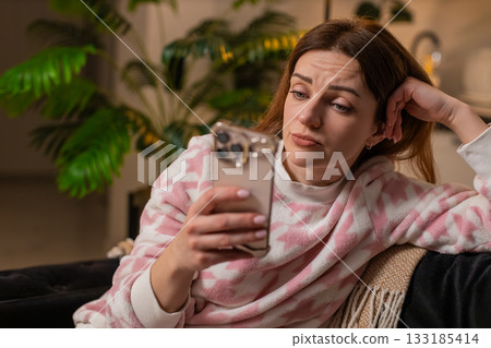 Adult woman scrolls phone news at night boredom sets in tired eyes stress demotivation sighs frowns Adult woman scrolls phone news at night boredom sets in tired eyes stress demotivation sighs frowns 133185414