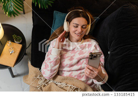 Adult woman with wireless headphones listens to music on smartphone eyes closed nods smiles gently Adult woman with wireless headphones listens to music on smartphone eyes closed nods smiles gently 133185415