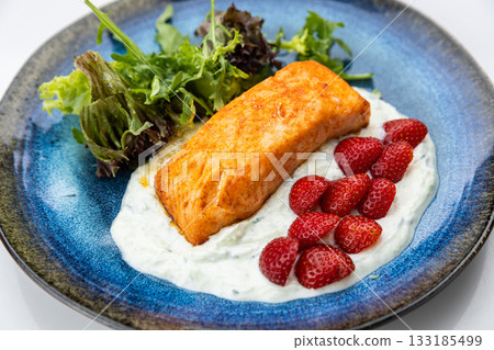 Seared salmon fillet with yogurt sauce, fresh strawberries and greens on blue ceramic plate 133185499