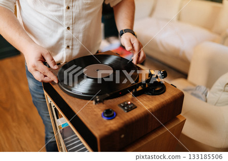 Placing a vinyl record on a wooden turntable at home, cozy audiophile moment Placing a vinyl record on a wooden turntable at home, cozy audiophile moment 133185506