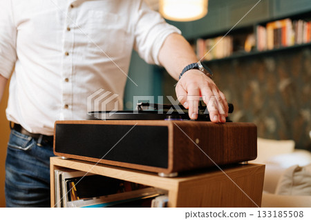 Hand lowering tonearm on vinyl record player, cozy home audio setup Hand lowering tonearm on vinyl record player, cozy home audio setup 133185508