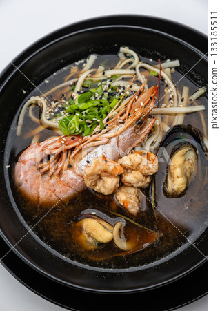 Seafood ramen with prawn, mussels and noodles in soy broth, black bowl on white background Seafood ramen with prawn, mussels and noodles in soy broth, black bowl on white background 133185511