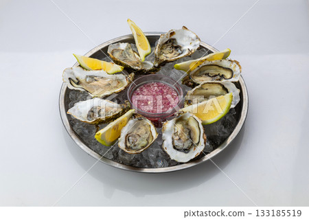 Fresh oysters on ice with lemon wedges and mignonette sauce on metal platter, top view Fresh oysters on ice with lemon wedges and mignonette sauce on metal platter, top view 133185519